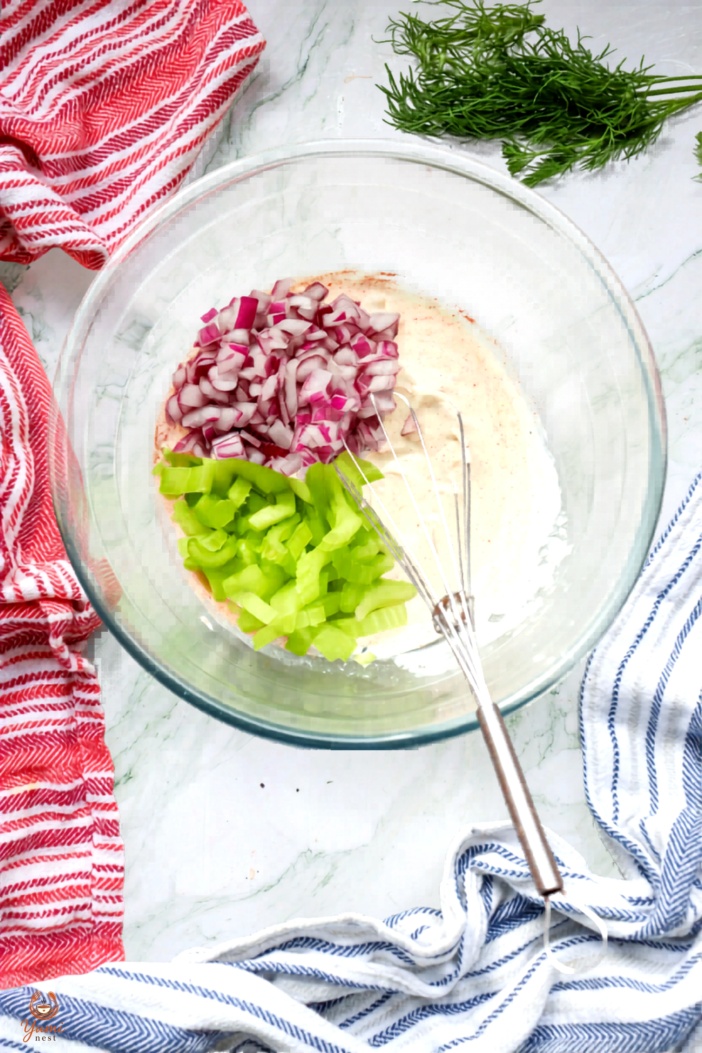 Celery and red onion added to the mayonnaise base in a glass bowl