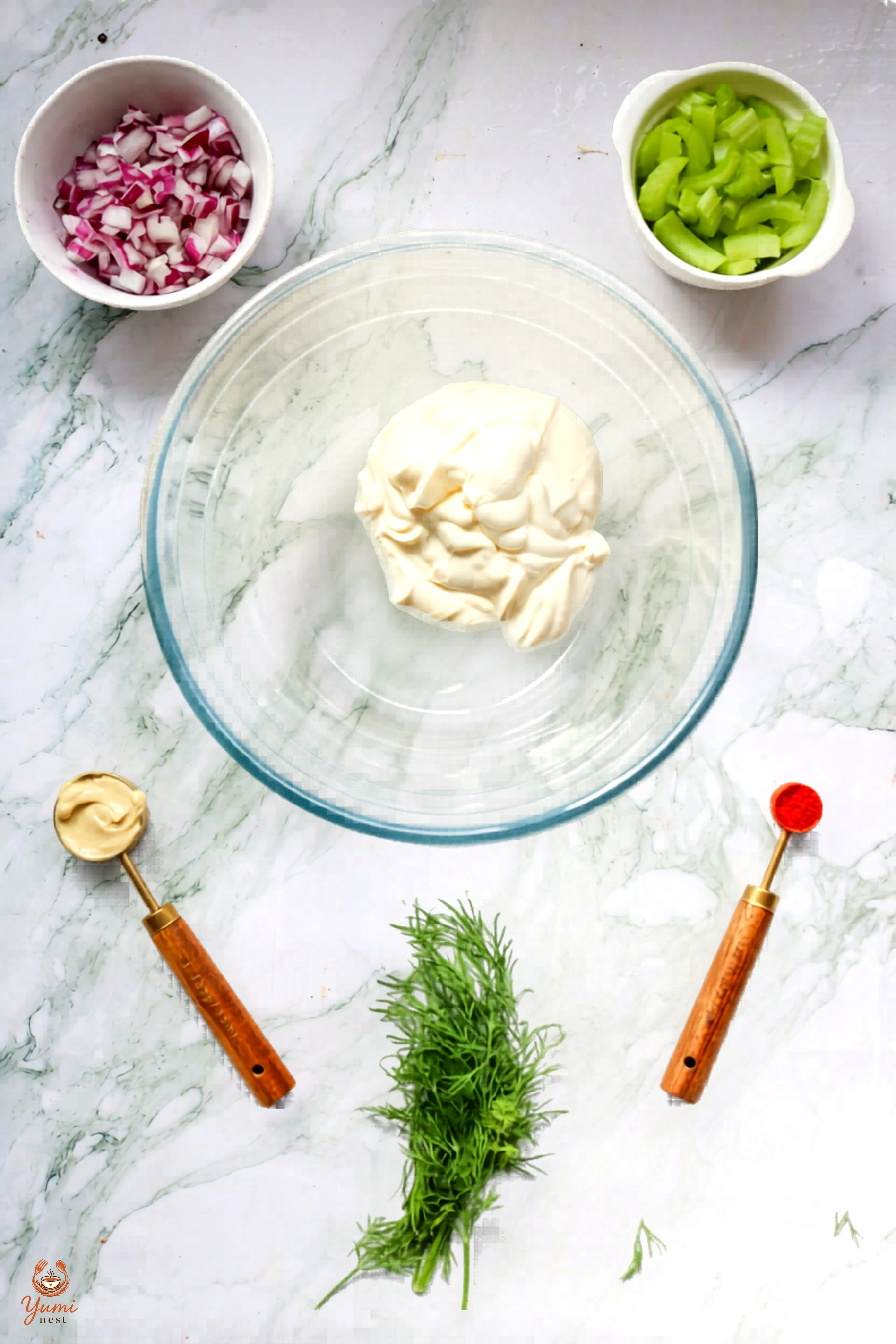 Mayonnaise in a glass mixing bowl with chopped onion and celery nearby