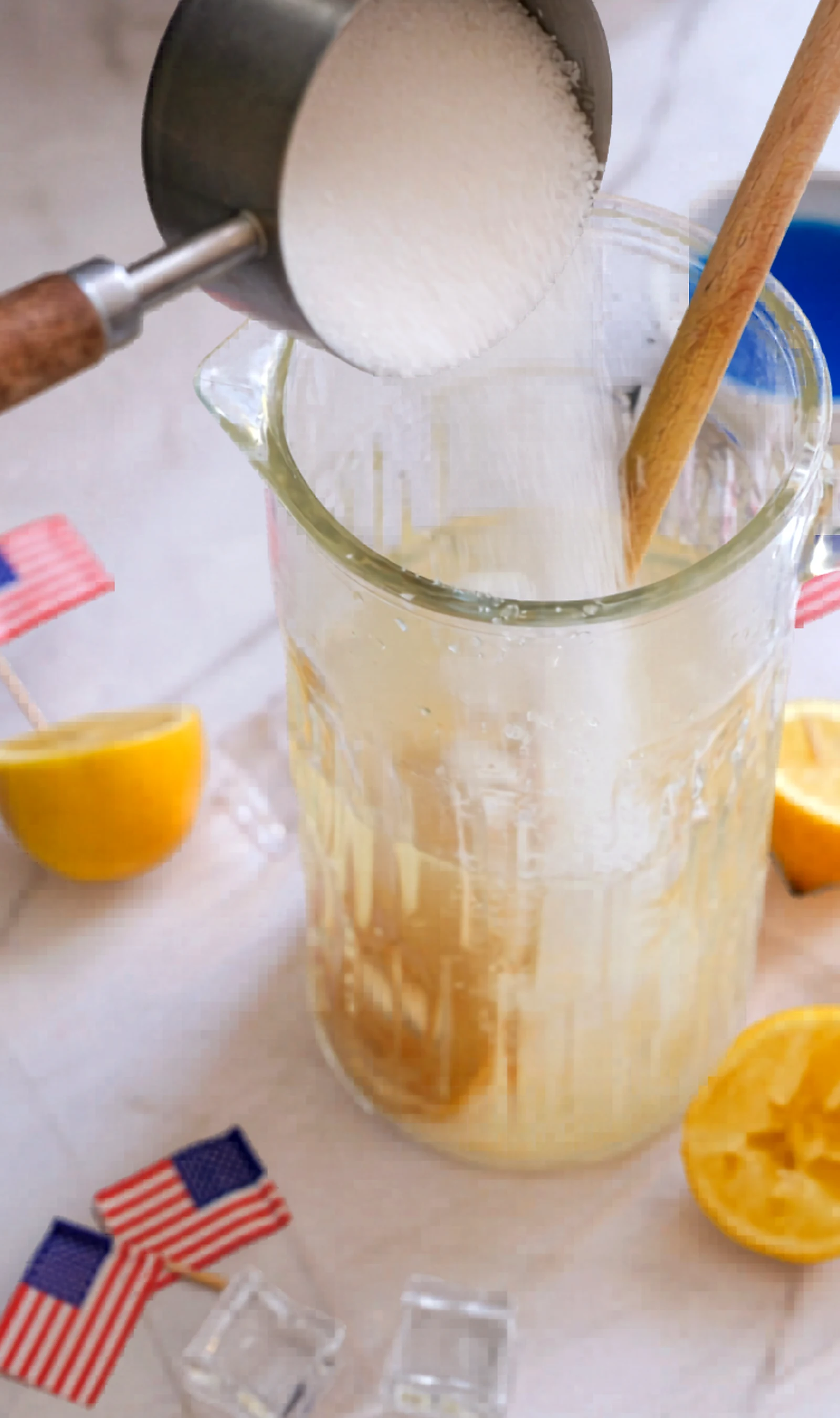 Granulated sugar being added to a lemon drink pitcher.