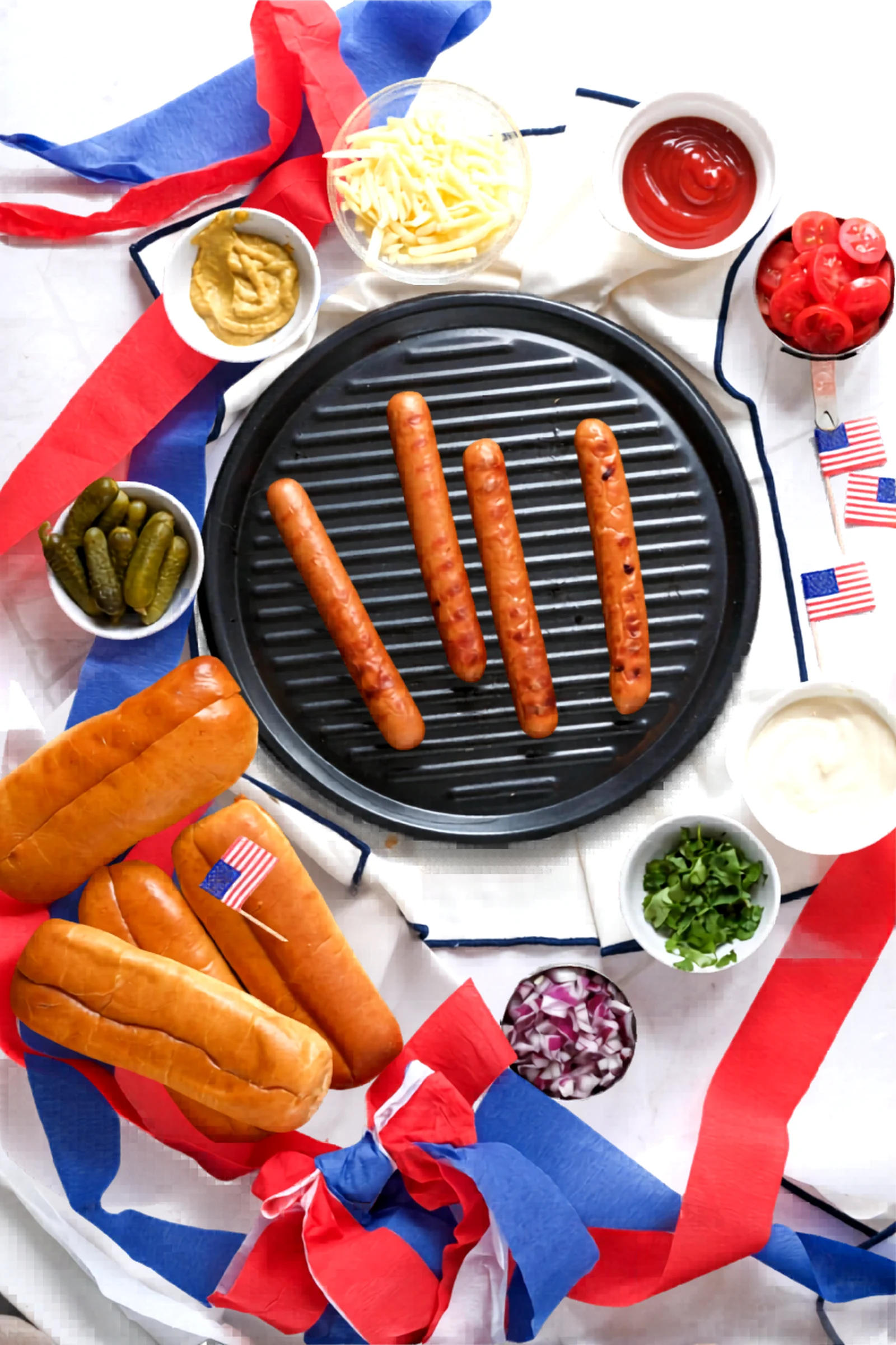 Ingredients and grilled hot dogs for Fourth of July hot dogs arranged around a grill pan.
