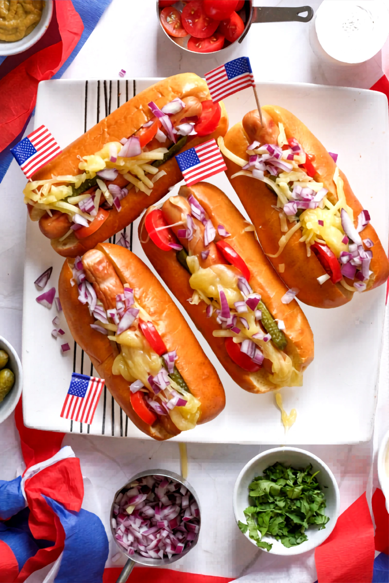 Hot dogs in buns topped with cheese, pickles, tomatoes, onion, and parsley.