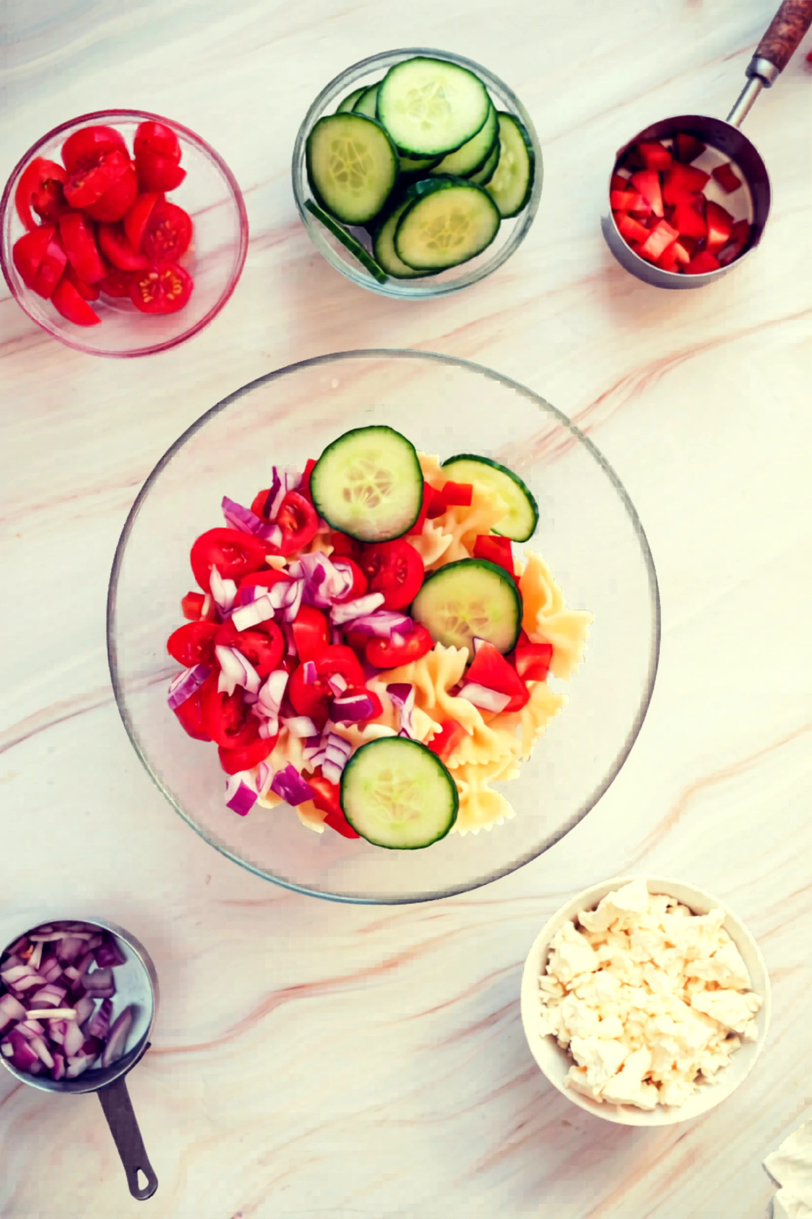 Pasta salad bowl with cucumbers and diced red onion added.