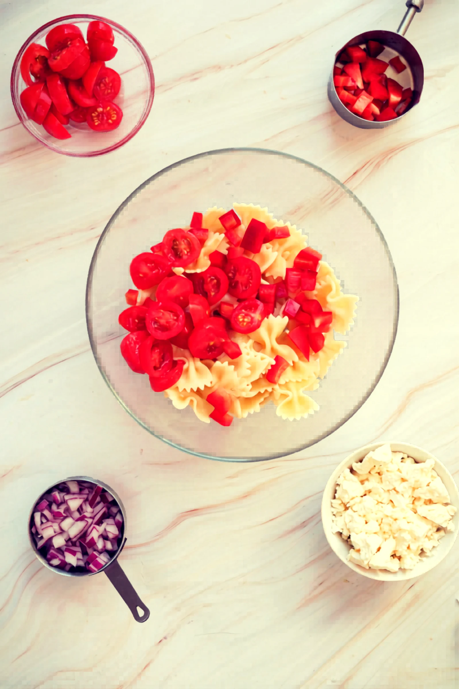 Bowtie pasta in a bowl with cherry tomatoes and diced red bell pepper.