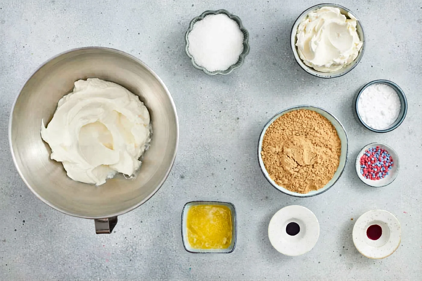 Ingredients for red white and blue mini no bake cheesecakes laid out on a gray surface