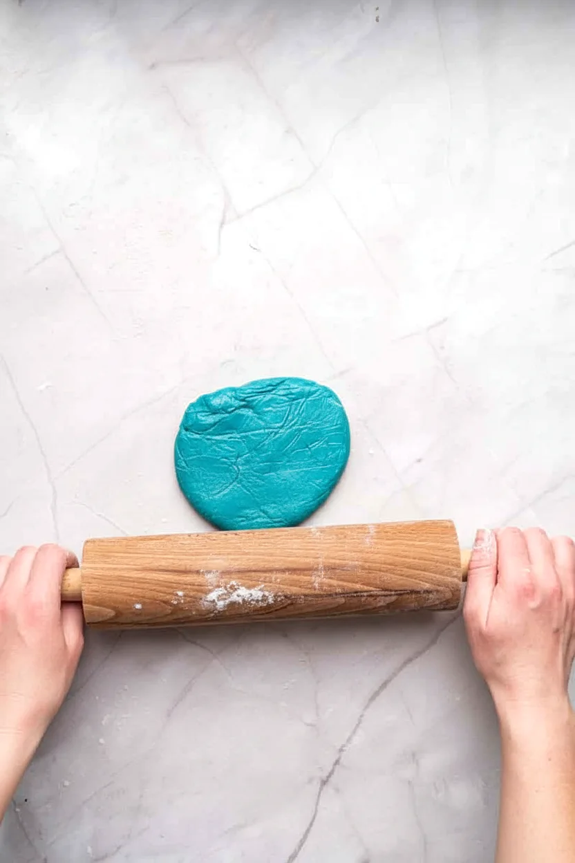 Blue cookie dough being rolled on parchment