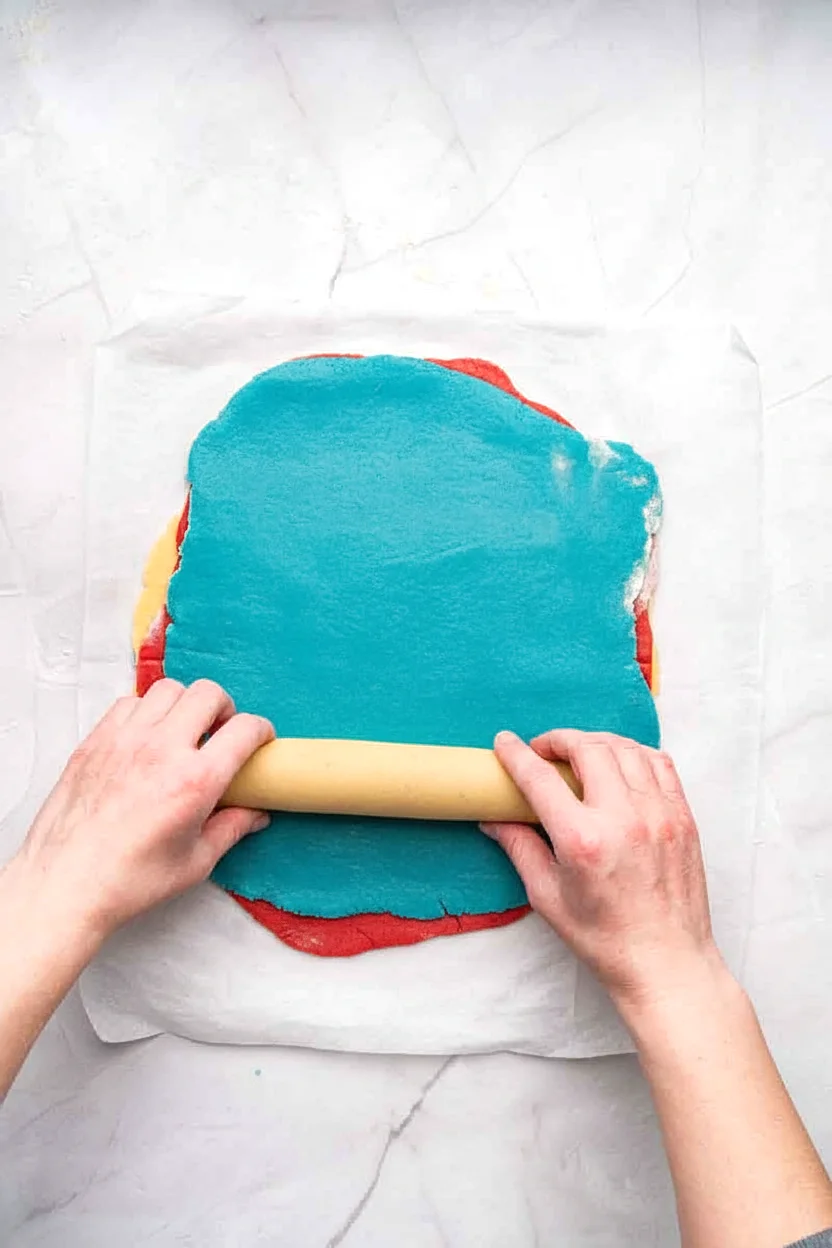 Layered red white and blue dough being rolled into a log