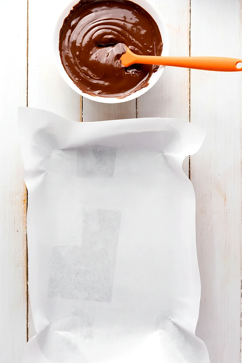 Melted dark chocolate beside a parchment lined pan for chocolate bark