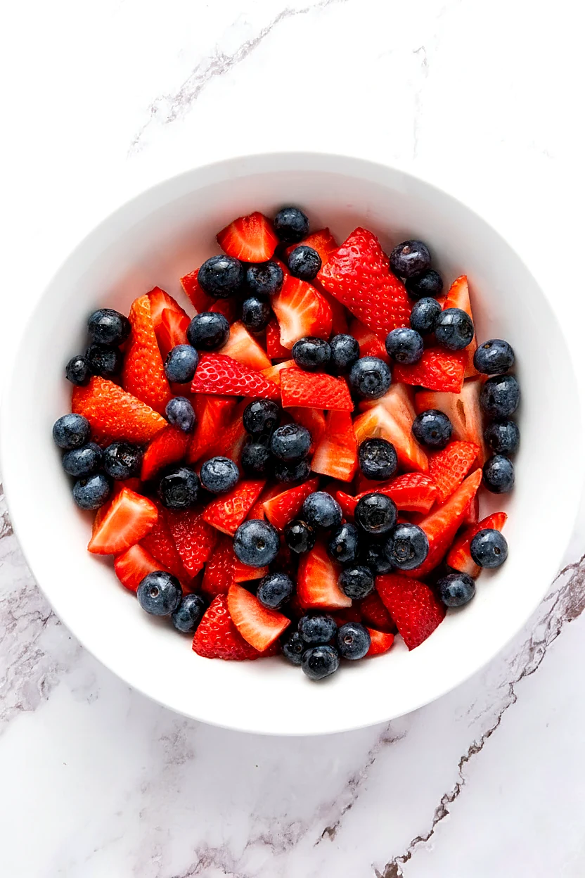 Strawberries and blueberries mixed in a white bowl for star spangled fruit salad