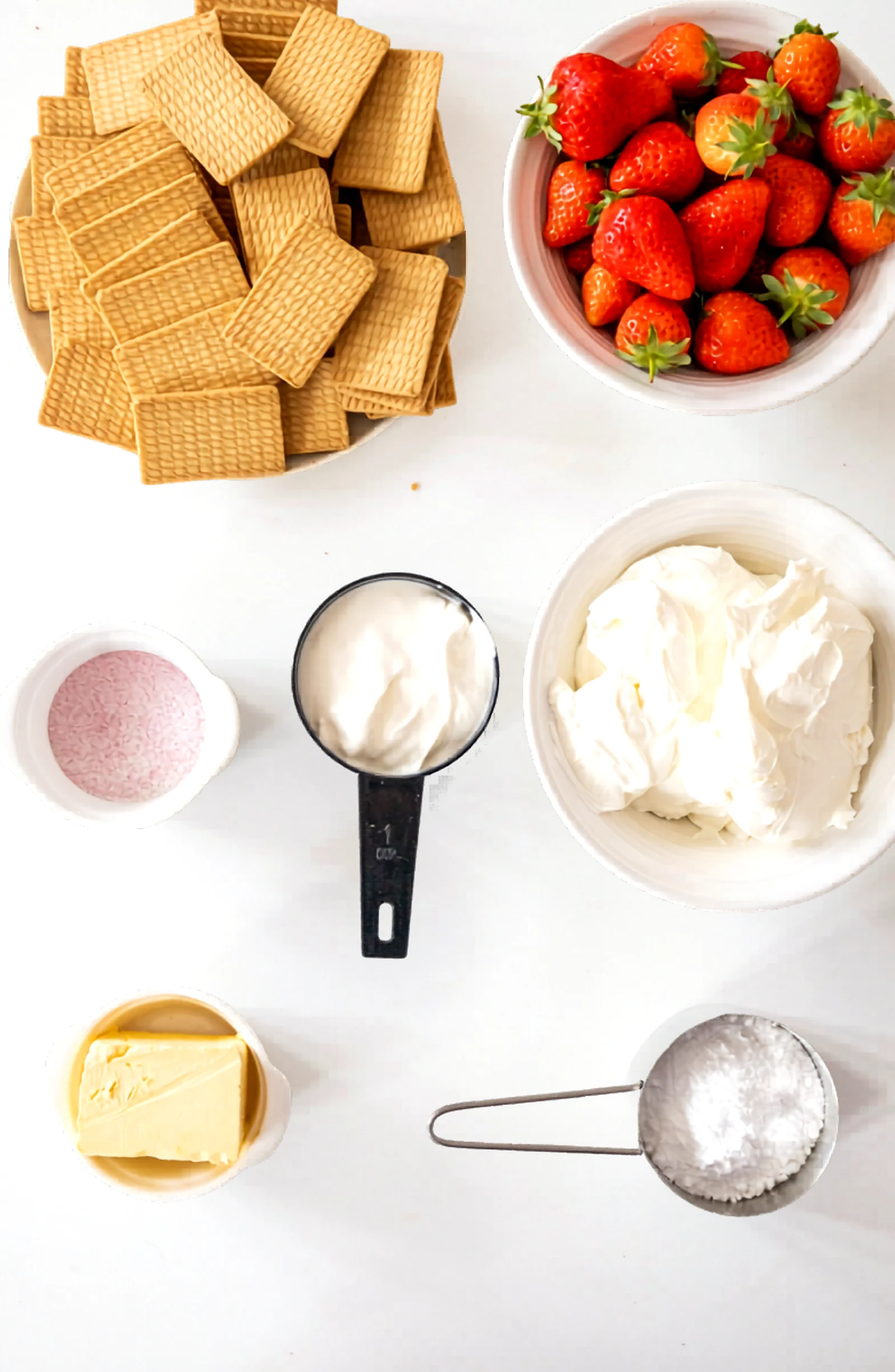 Ingredients for strawberry no bake cheesecake laid out on a white surface.