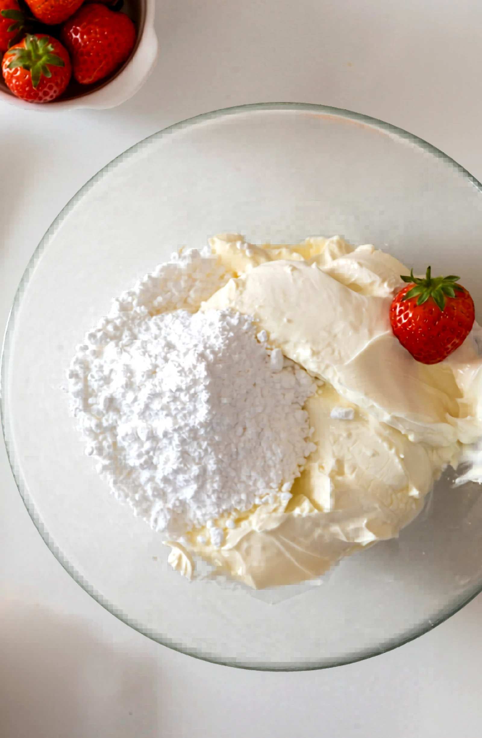Cream cheese and powdered sugar in a glass mixing bowl.
