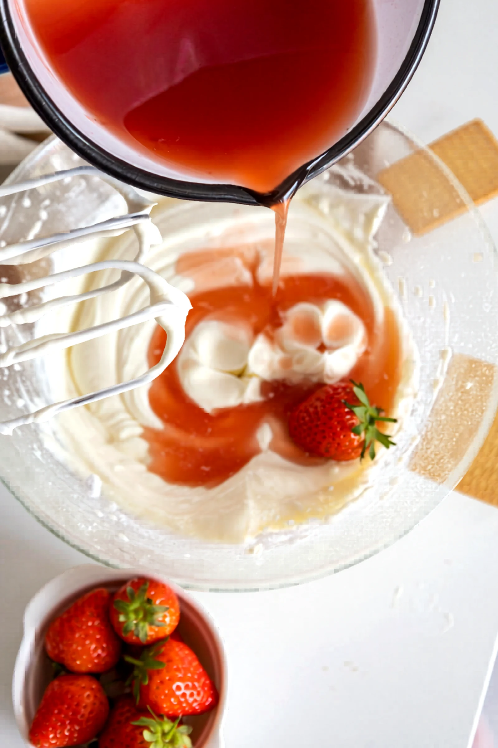 Strawberry gelatin mixture being poured into the cheesecake filling.