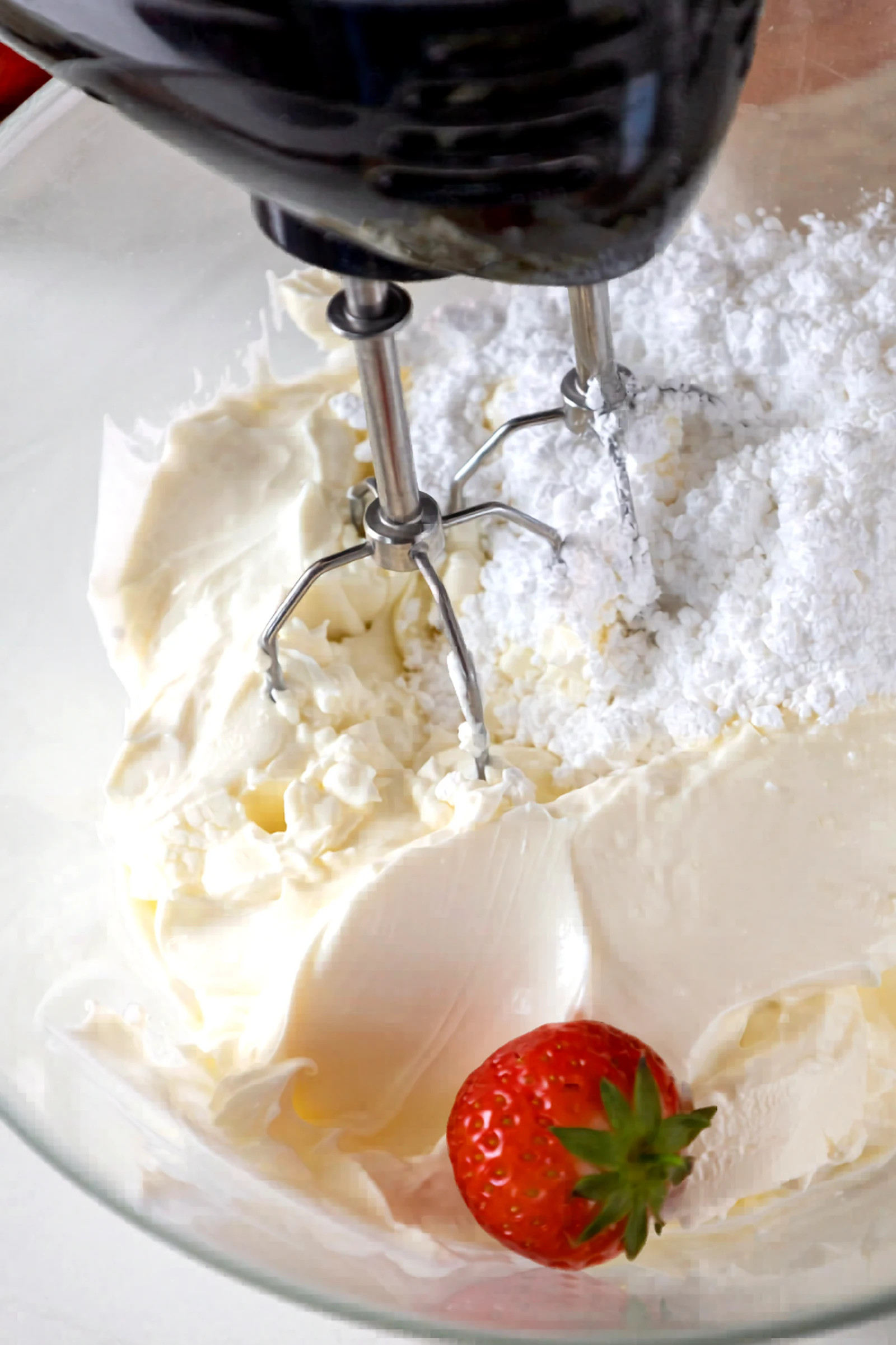 Mixer beating the cheesecake filling base in a glass bowl.