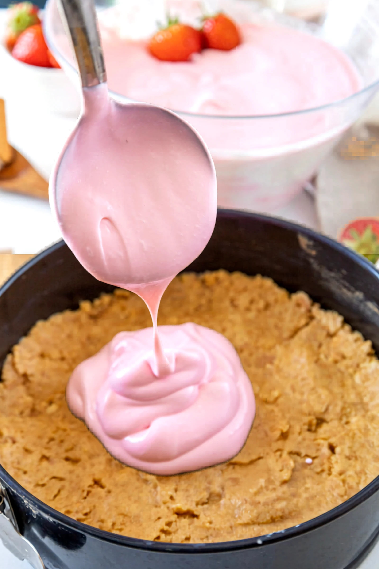 A spoonful of pink cheesecake filling being added to the crust.