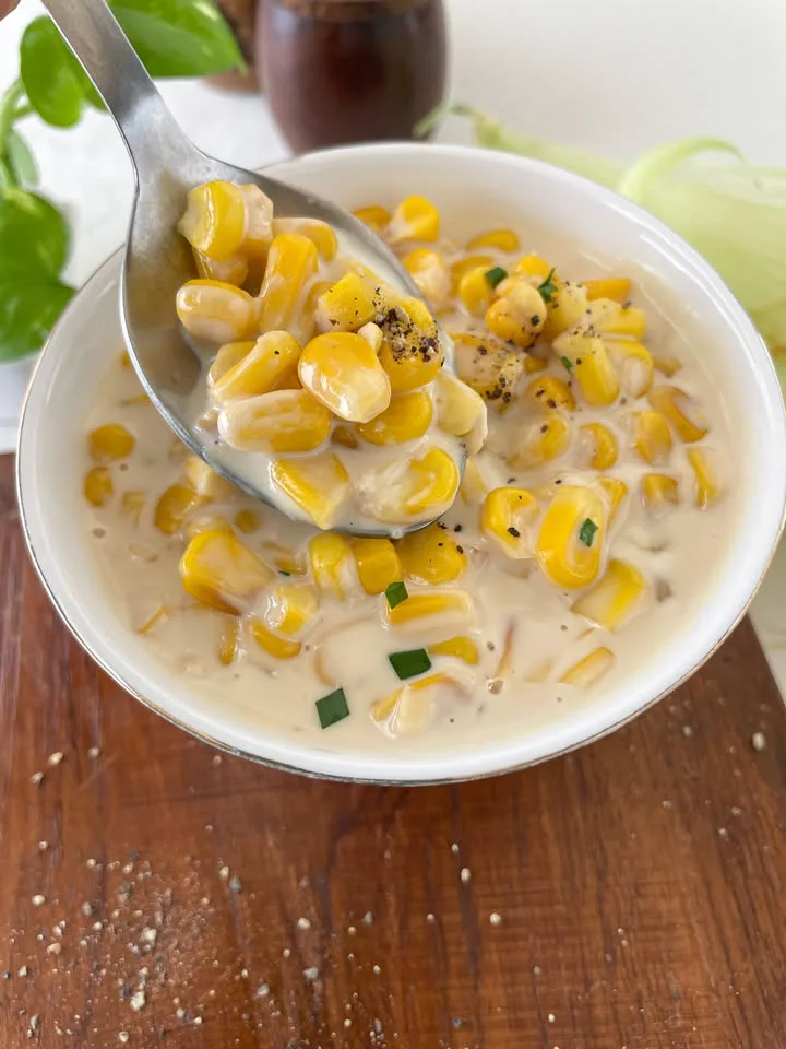 Finished creamed corn with pepper in a white serving bowl