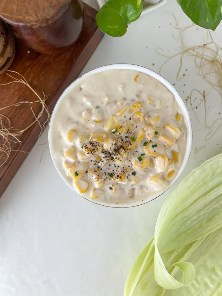 Bowl of creamy corn garnished with black pepper and chives viewed from above