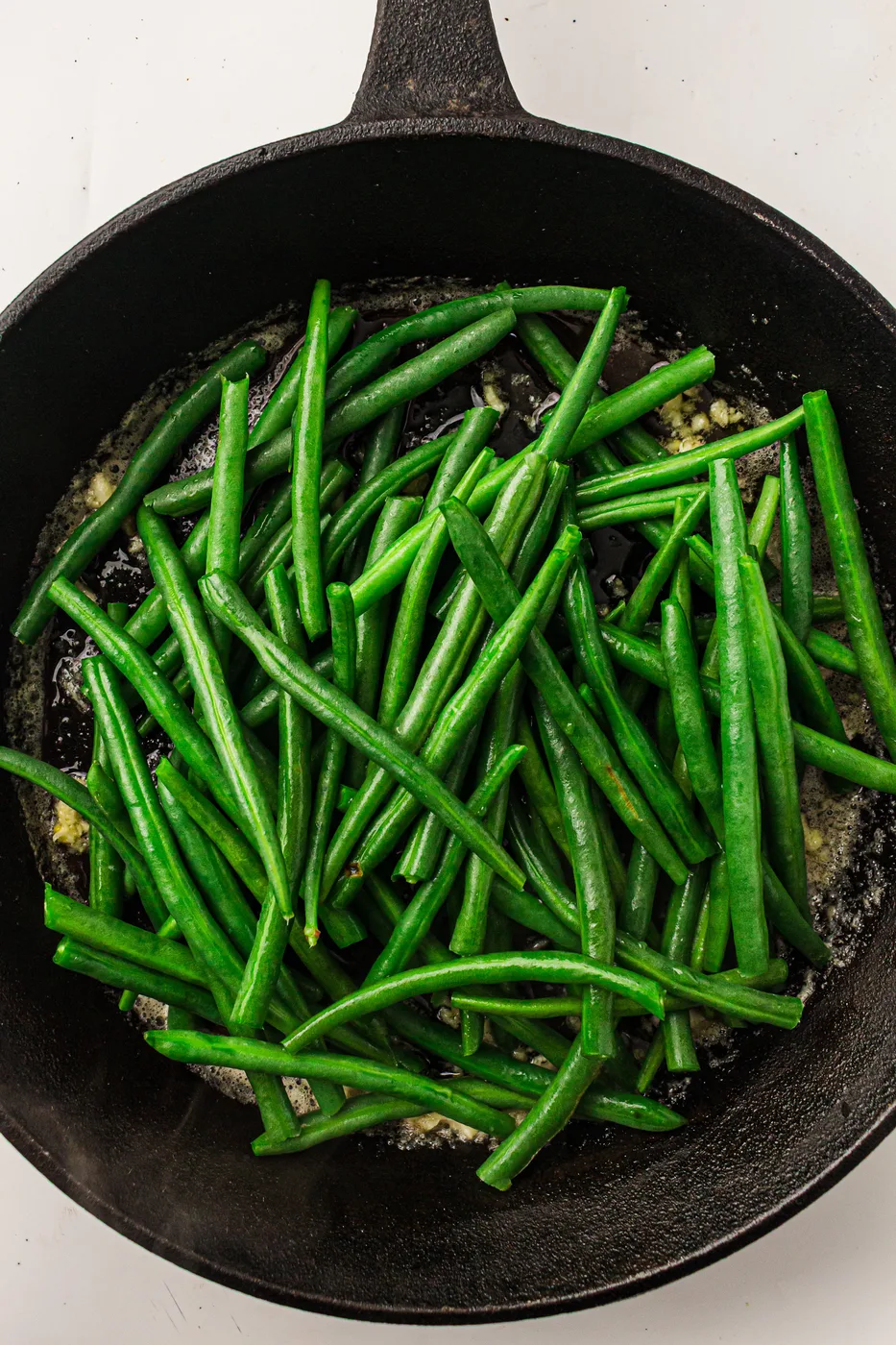 Blanched green beans tossed with garlic butter in a skillet
