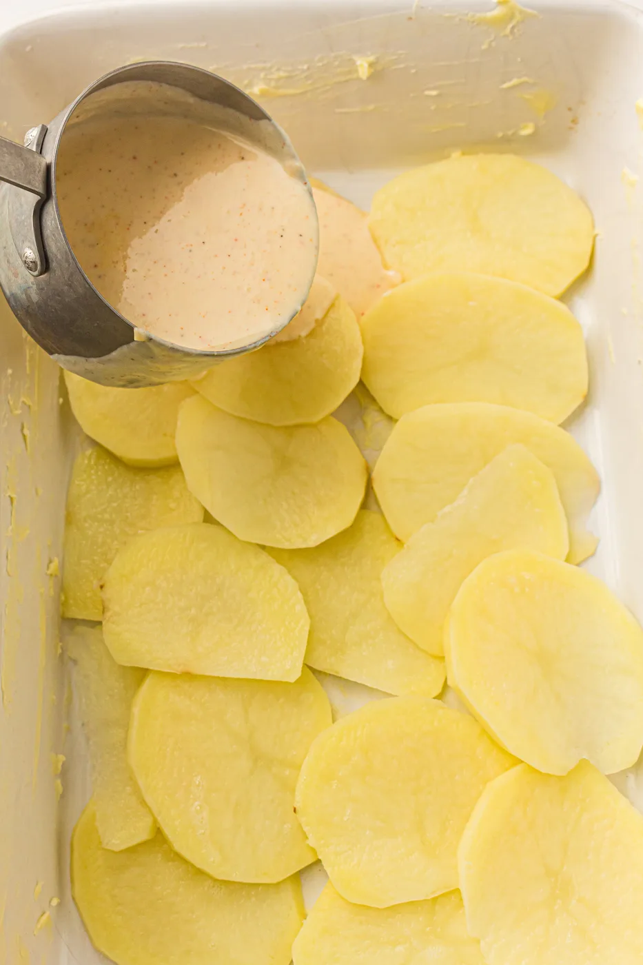 Cream sauce poured over thinly sliced potatoes in a baking dish
