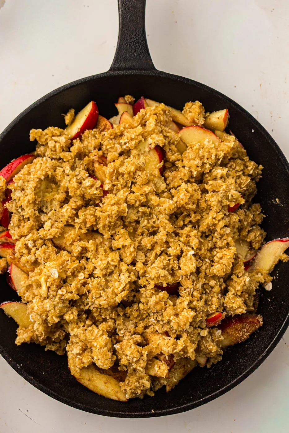 Unbaked apple crisp assembled with oat topping in a cast-iron skillet